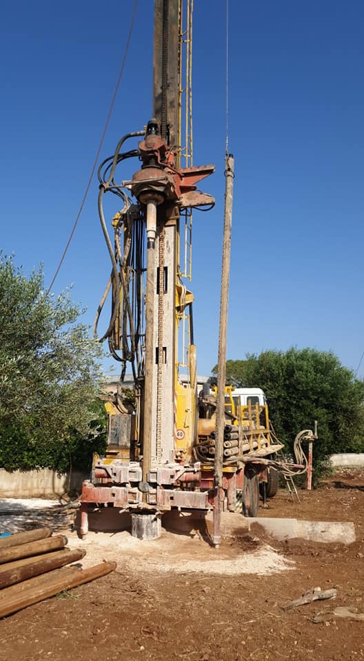 Piattaforma di perforazione in un cantiere edile; gialla e beige con cielo blu, tubo di perforazione visibile, tronchi a terra.