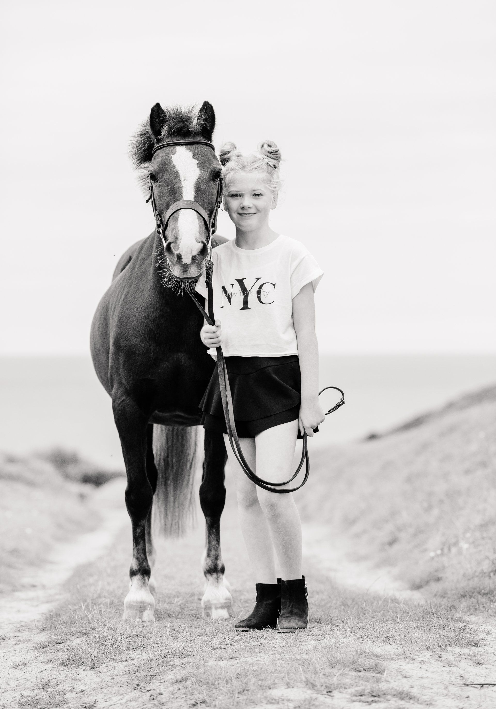 Girl with space buns and a pony, standing on a dirt path with the ocean in the background.