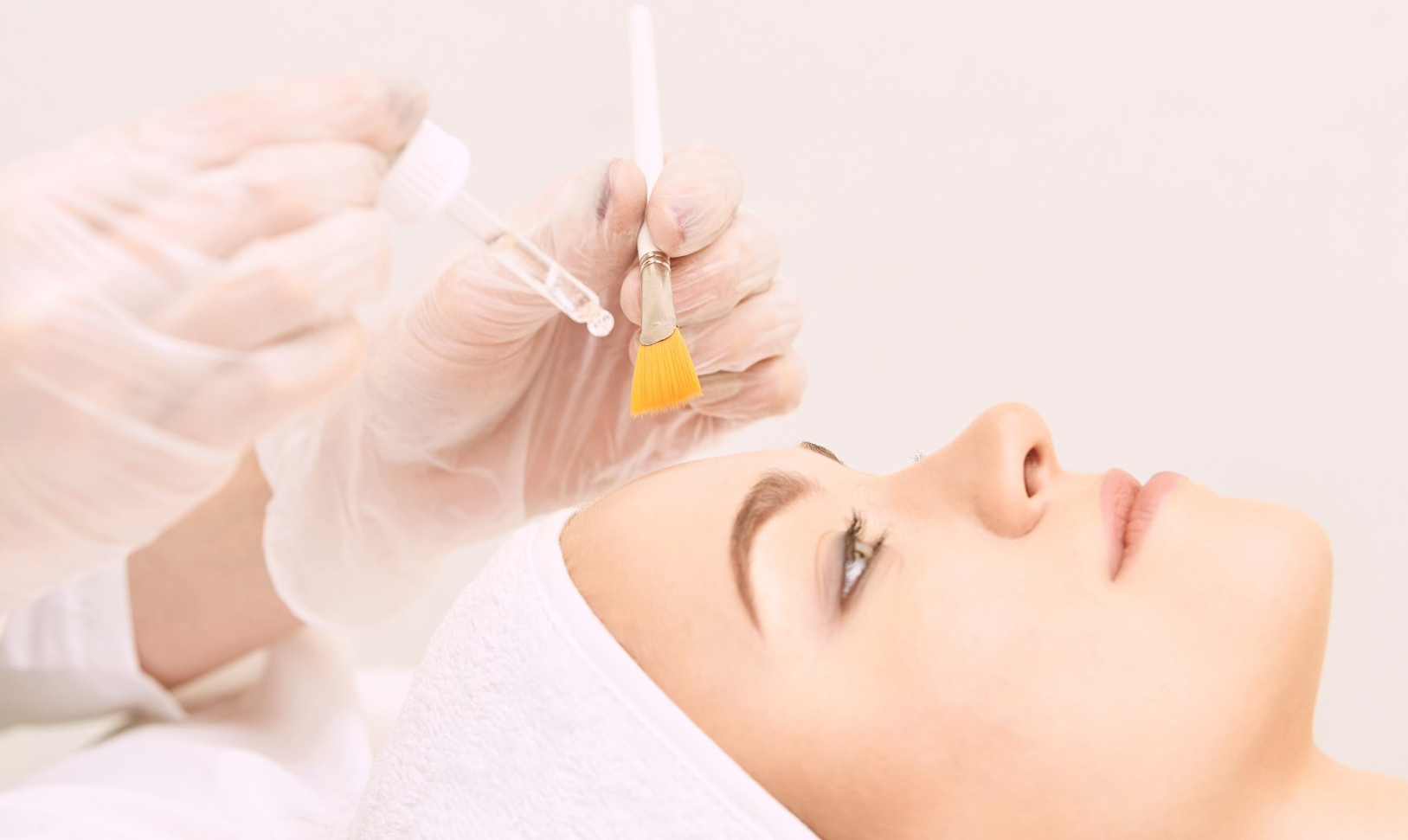 A facial treatment applying serum to a woman’s face with a dropper, in a bright spa setting