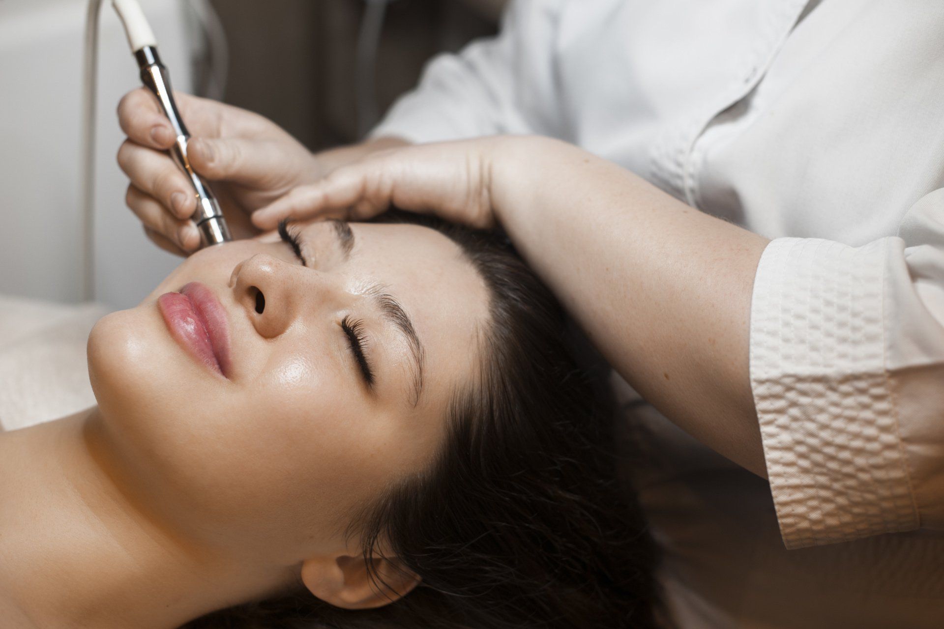 Cosmetician applying treatment to a woman’s face with a handheld device in a spa setting