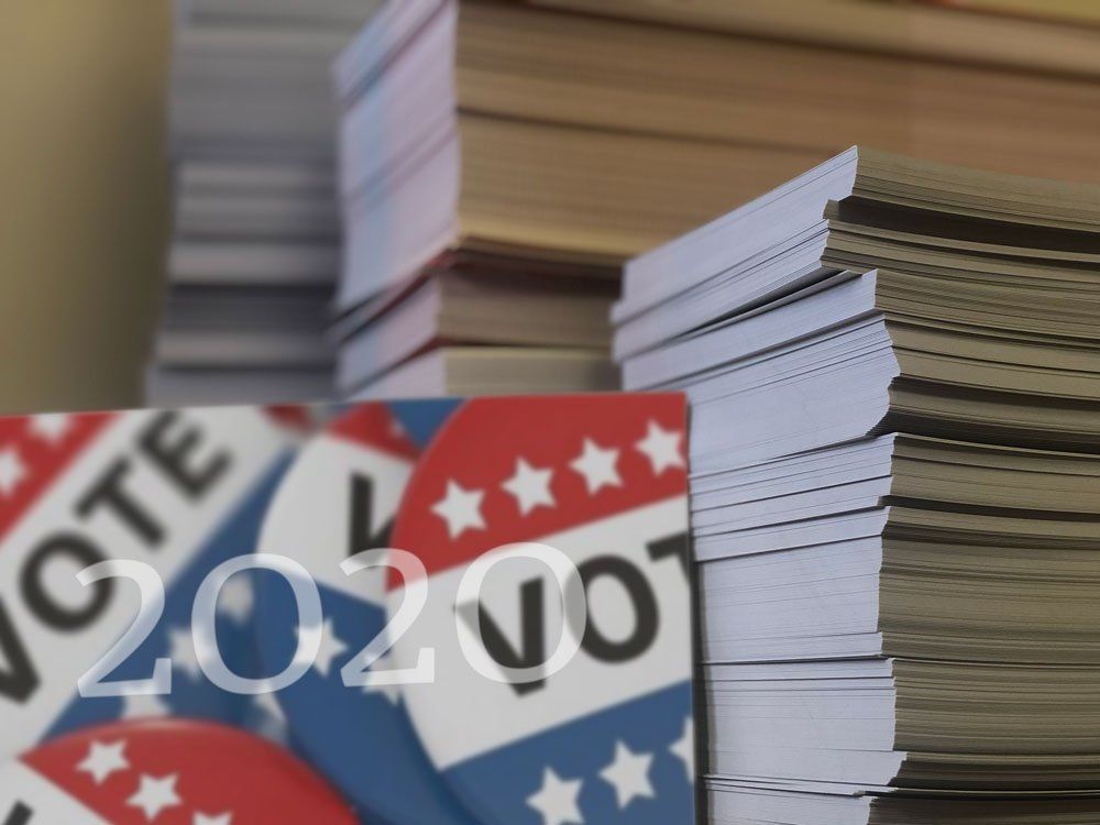 Stack of voting pamphlets with red, white, and blue “vote” signs and a 2020 ballot number label.