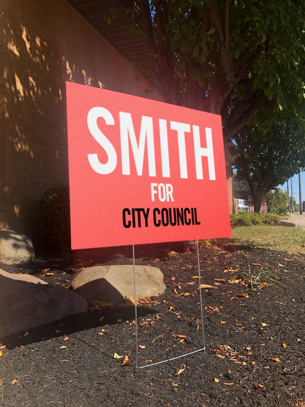 Red political yard sign reading “SMITH FOR CITY COUNCIL” beside a sidewalk and landscaping.