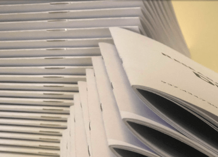 Stack of white magazines or reports with a window blind in the background