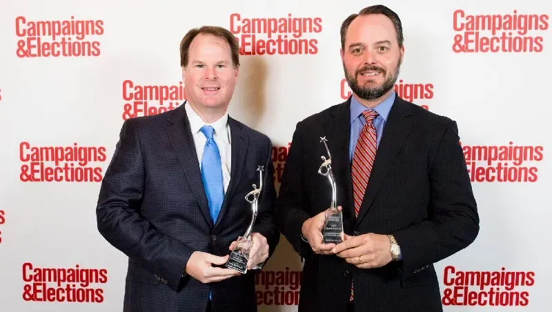 Two men holding awards, posing in front of a backdrop with 