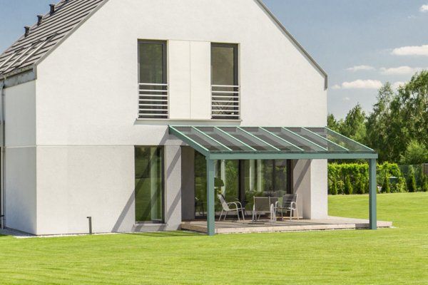A modern white house with a green-framed glass patio roof and outdoor seating set on a manicured lawn.