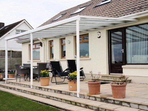 A white metal patio cover extends over a tiled terrace with outdoor furniture and potted plants