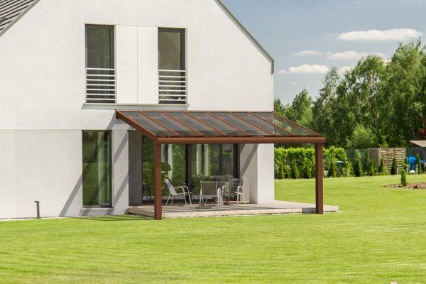 Modern white house with a brown patio canopy, sliding glass doors, and outdoor seating on a grassy lawn.