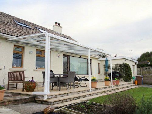 A white patio cover attached to a residential house with outdoor furniture on a tiled terrace.