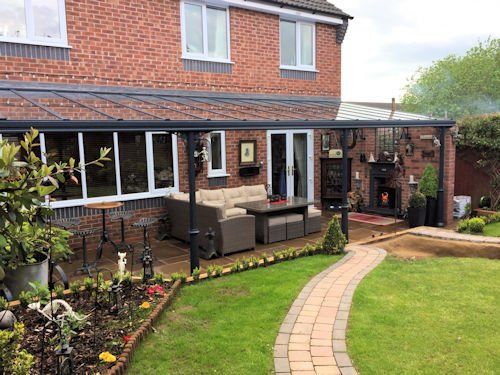 A brick house featuring a dark grey modern patio cover over a seating area with outdoor furniture and a fireplace.