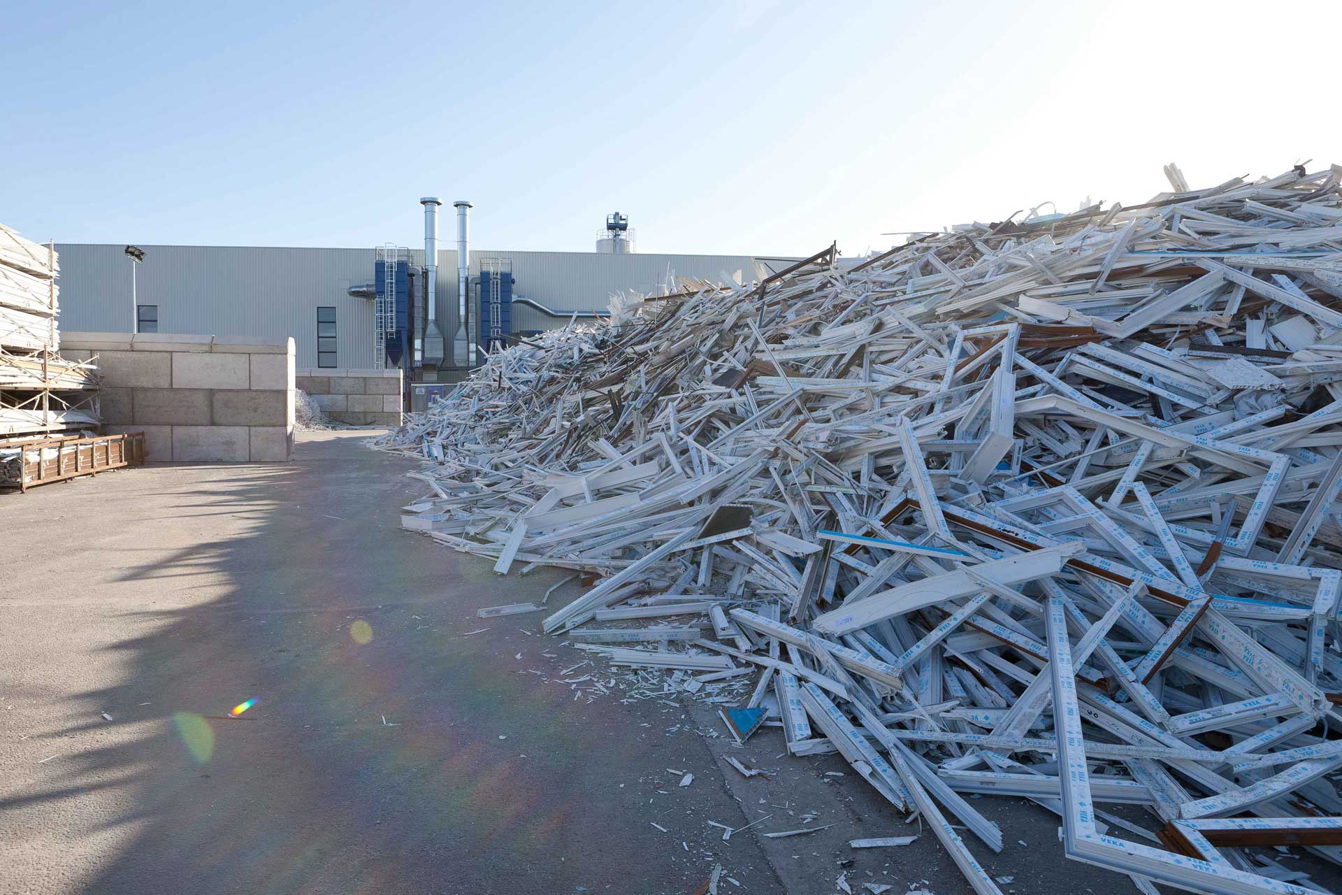 A large pile of white scrap wood and debris sits on the ground in front of an industrial building.