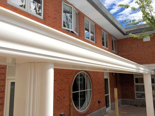 A brick building featuring a long, white curved awning supported by pillars, with rectangular and circular windows.