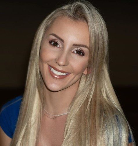 A woman with long blonde hair is smiling and wearing a blue shirt.