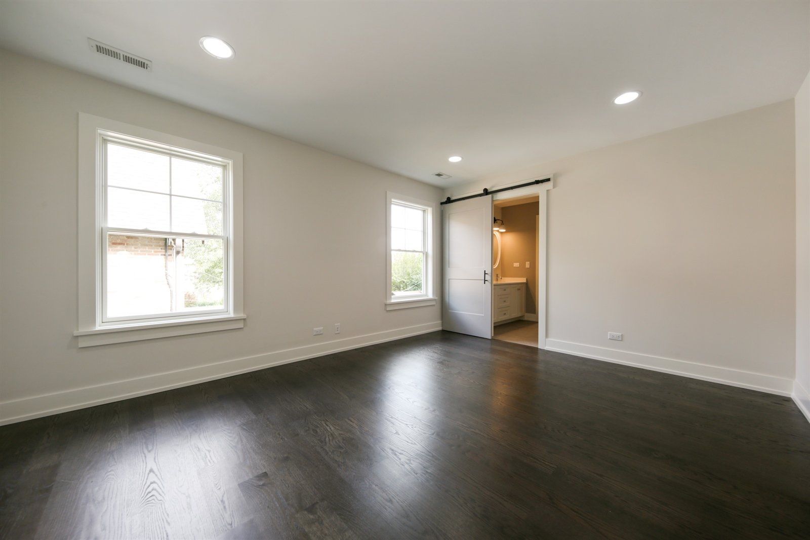 A large empty room with hardwood floors and two windows.