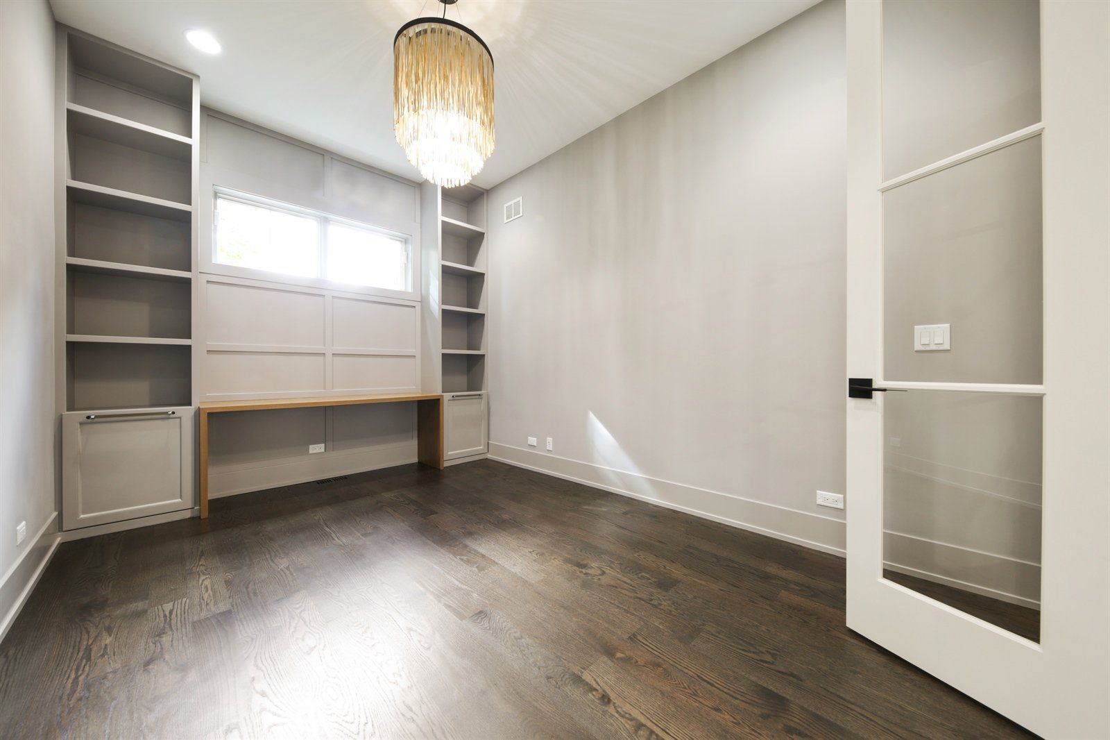 An empty room with a desk and shelves and a chandelier hanging from the ceiling.