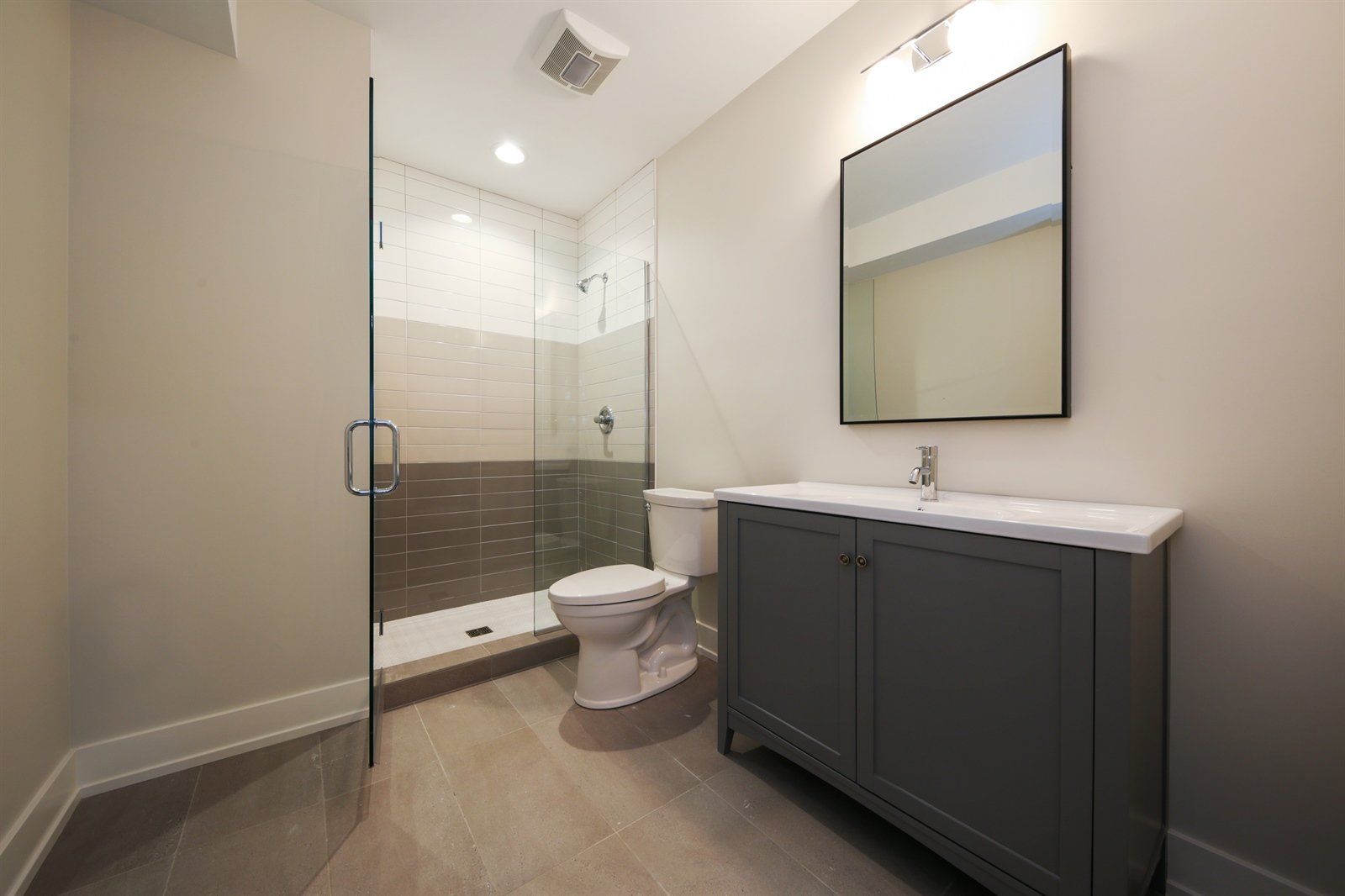 A bathroom with a toilet , sink , mirror and walk in shower.