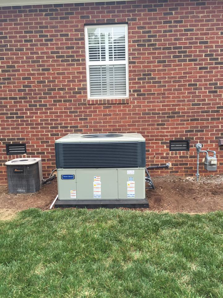 An air conditioning unit and a small gray box against a red brick wall, next to a gas meter.