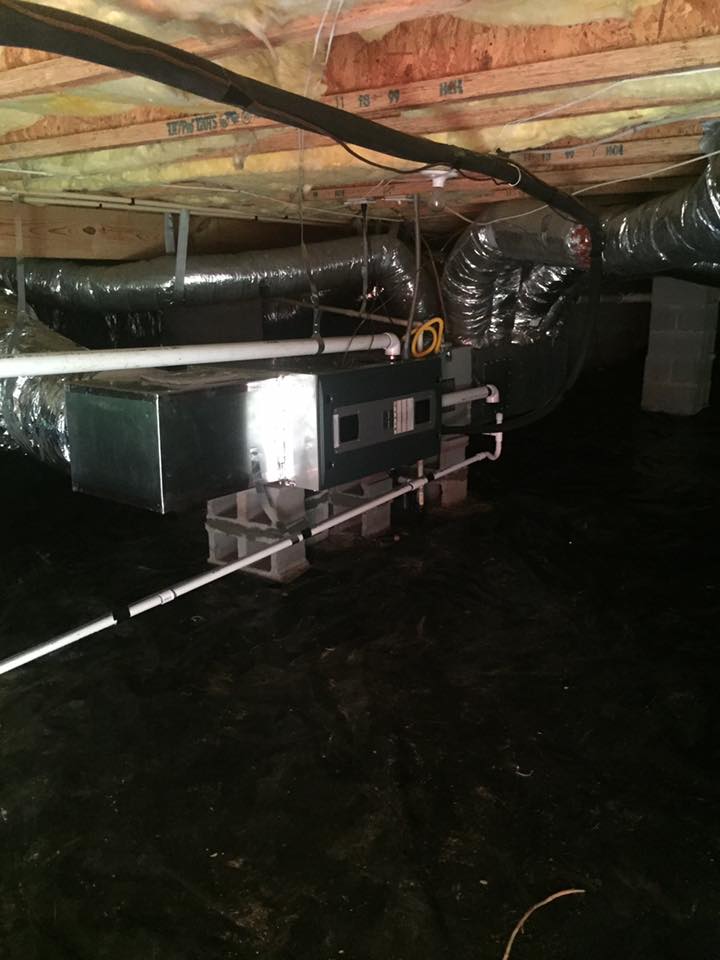 HVAC system in a crawlspace; black vapor barrier on ground, ductwork, wooden beams.