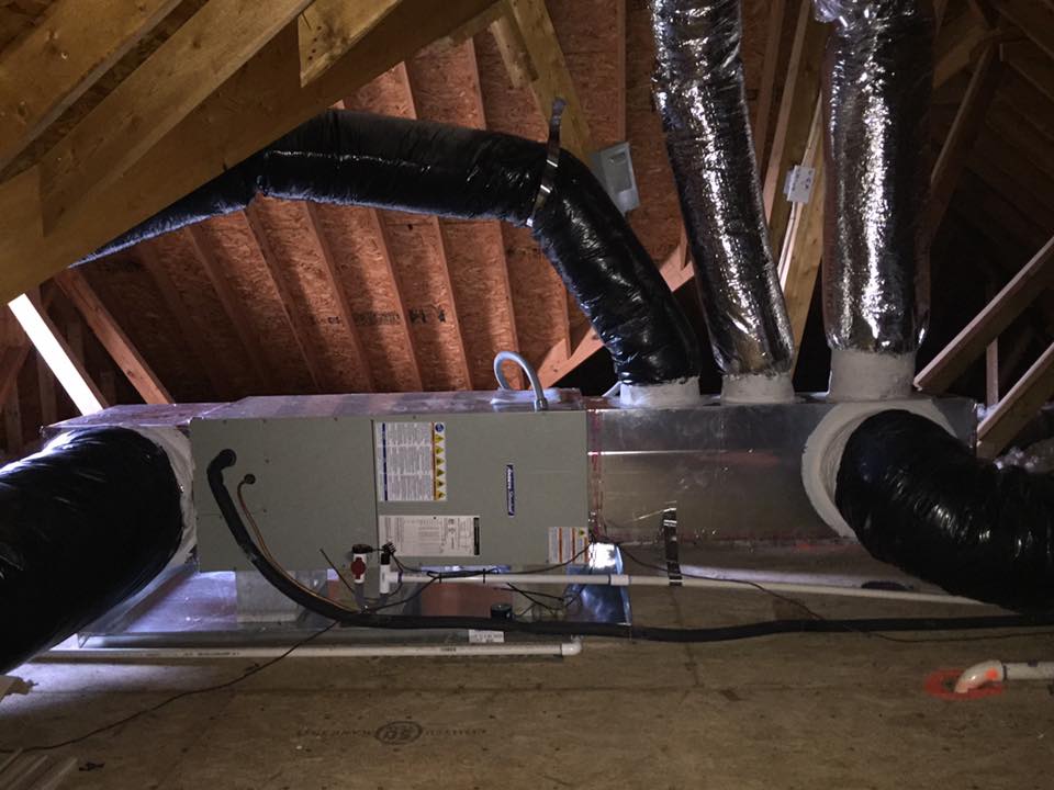 HVAC system in an attic with ductwork, gray unit, black insulated ducts, wood beams, and a white, unfinished floor.