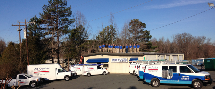 A company with multiple service vehicles parked outside a building, with a group of people standing on the roof.