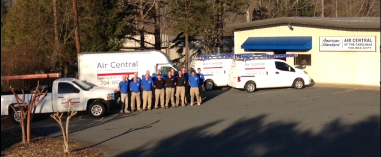 Group of workers in blue shirts and tan pants with company vans and building.