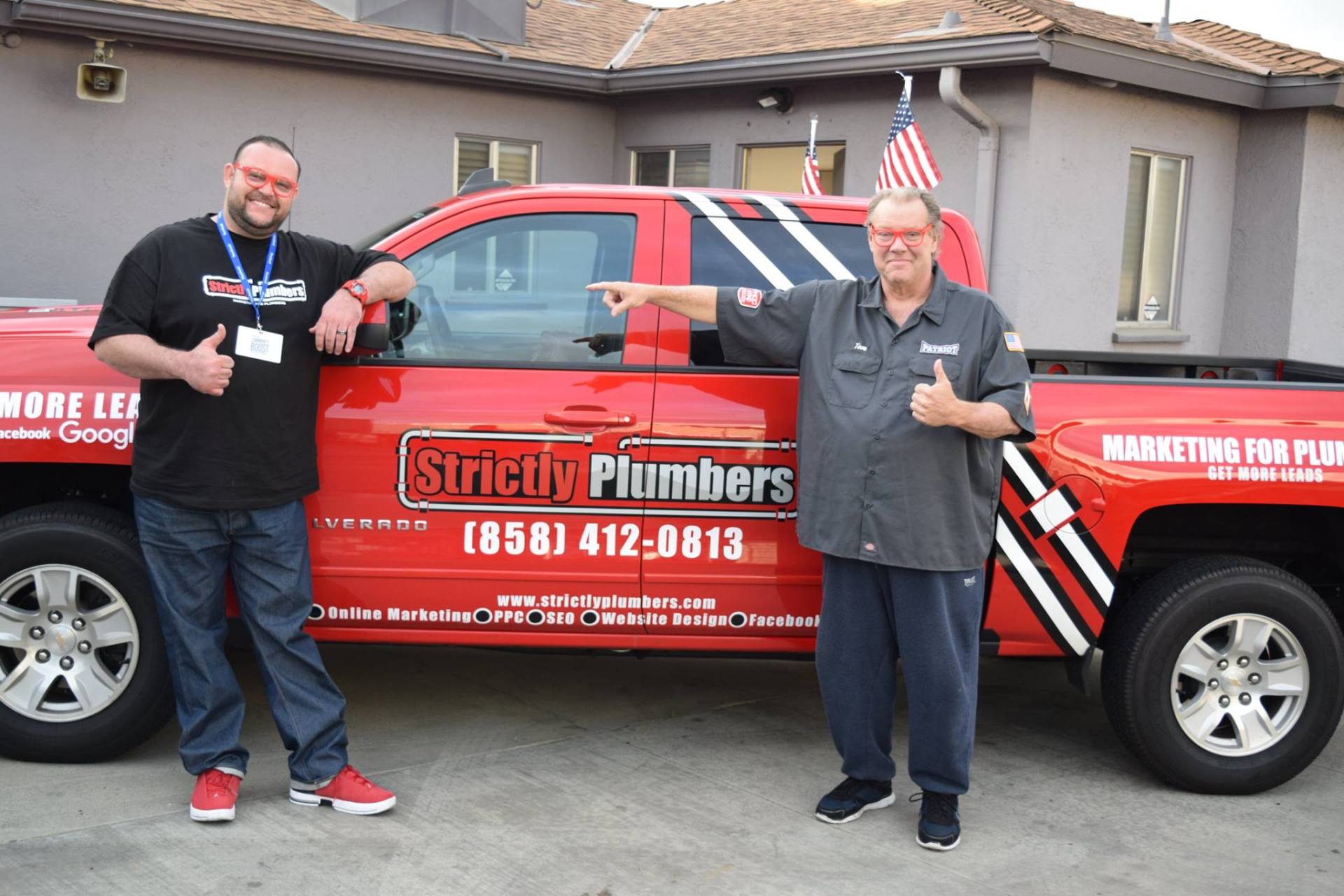 Two men standing next to a red truck that says strictly plumbers