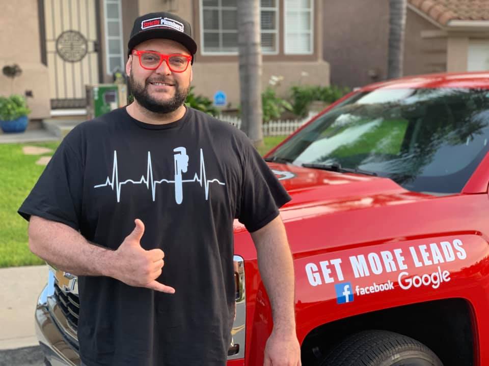 A man is standing in front of a red truck that says get more leads on it.