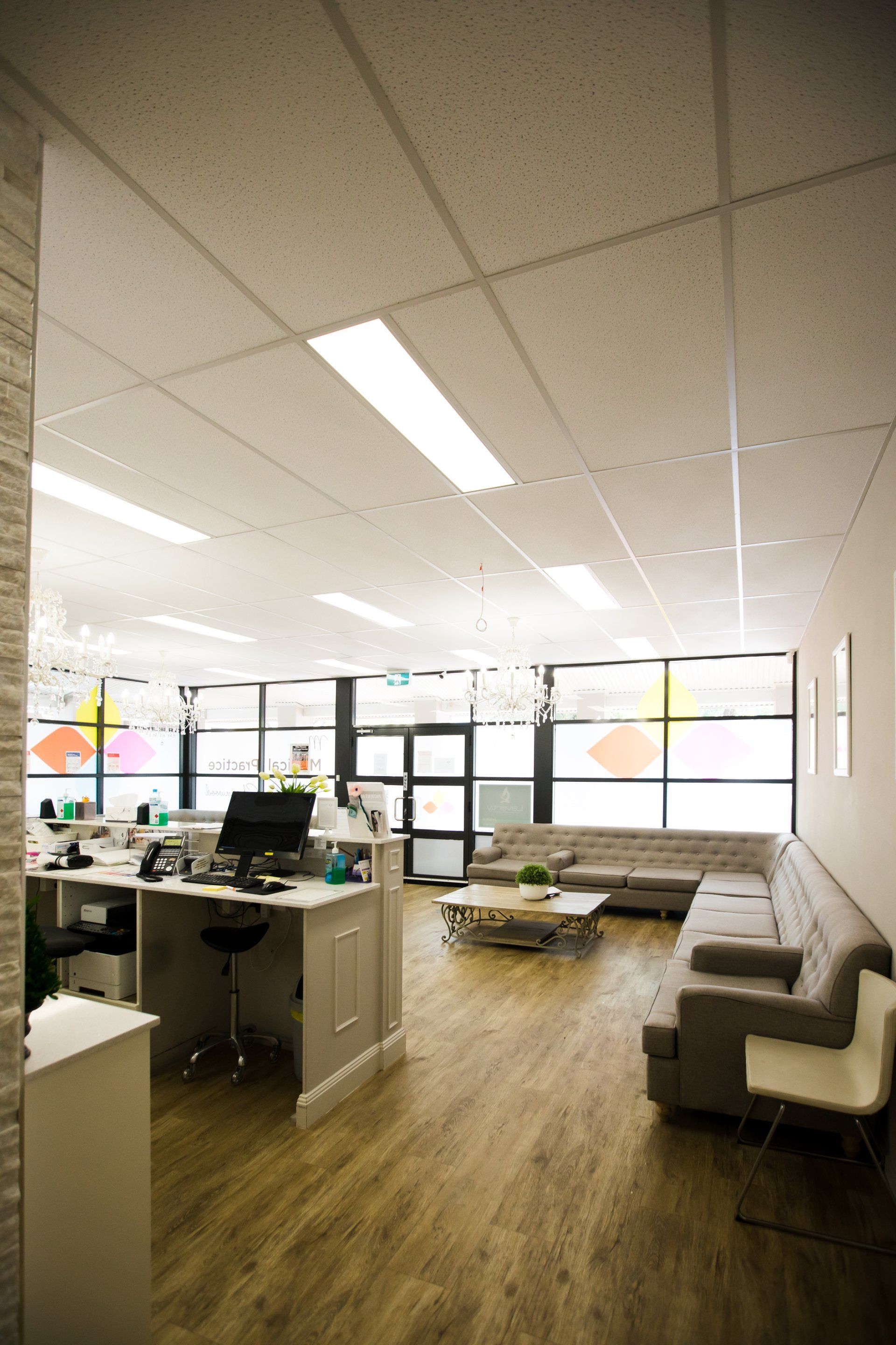 Modern office lounge with desks, white sofas, wood floors, and large windows letting in daylight