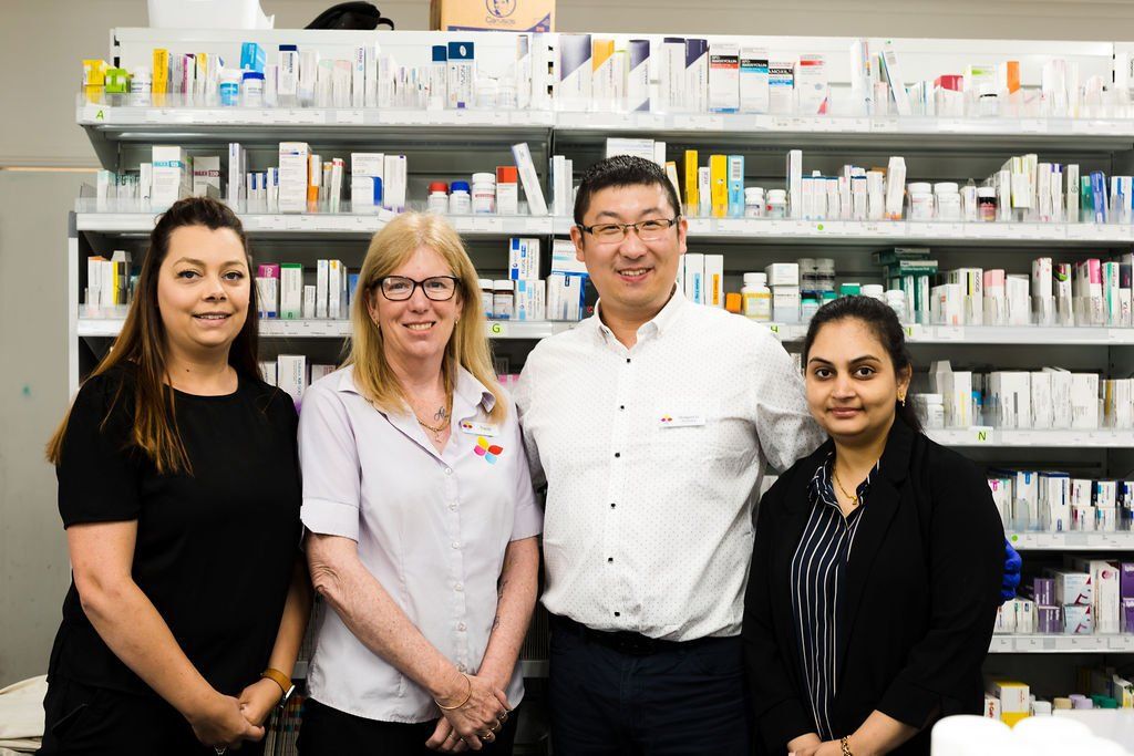 Four pharmacy staff standing in front of shelves of medication and supplies