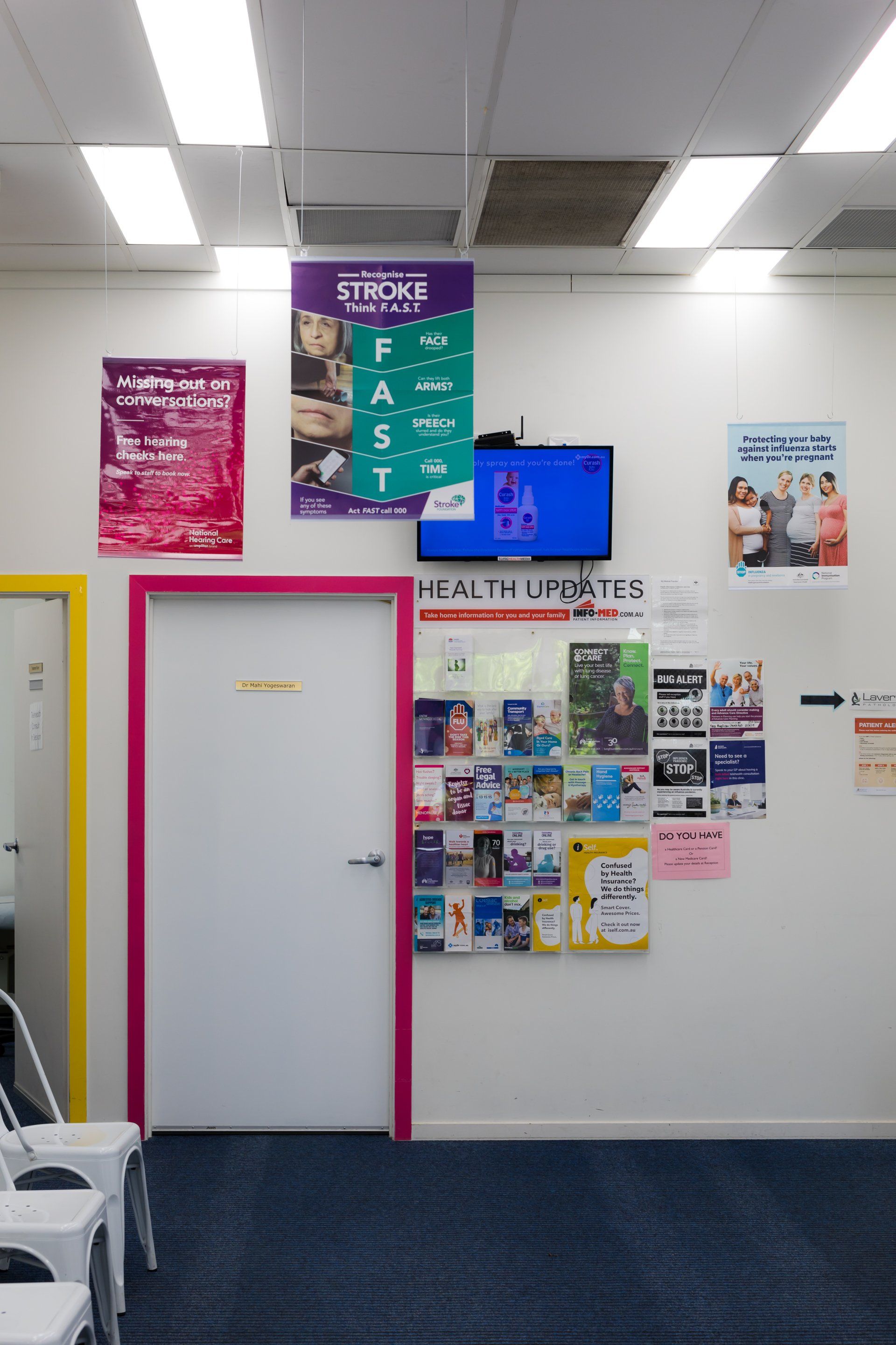 Clinic hallway with a white door outlined in pink and bulletin boards of health posters and updates