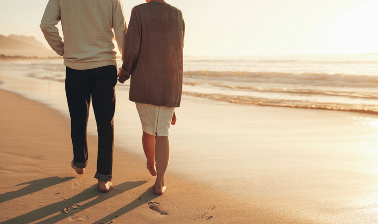 A man and a woman are walking on the beach holding hands.