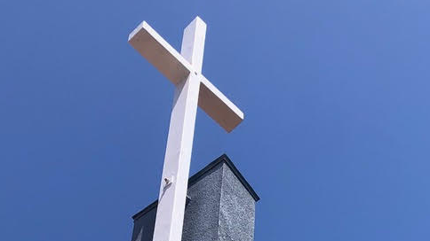 White cross atop a church steeple against a clear blue sky