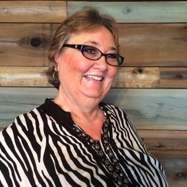 Smiling woman in glasses wearing a zebra-print top against a wooden plank wall