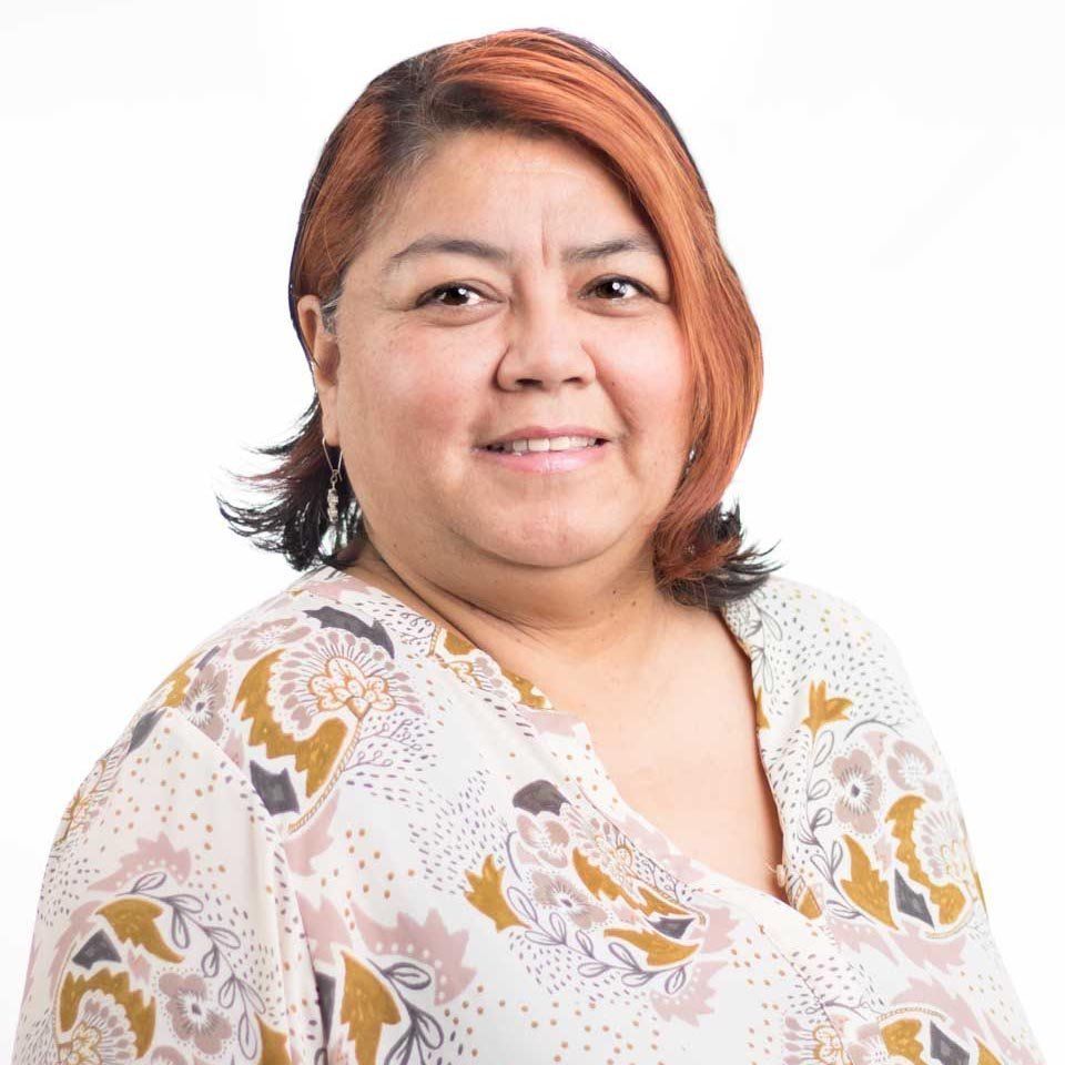 Smiling person with short auburn hair wearing a white patterned blouse on a white background