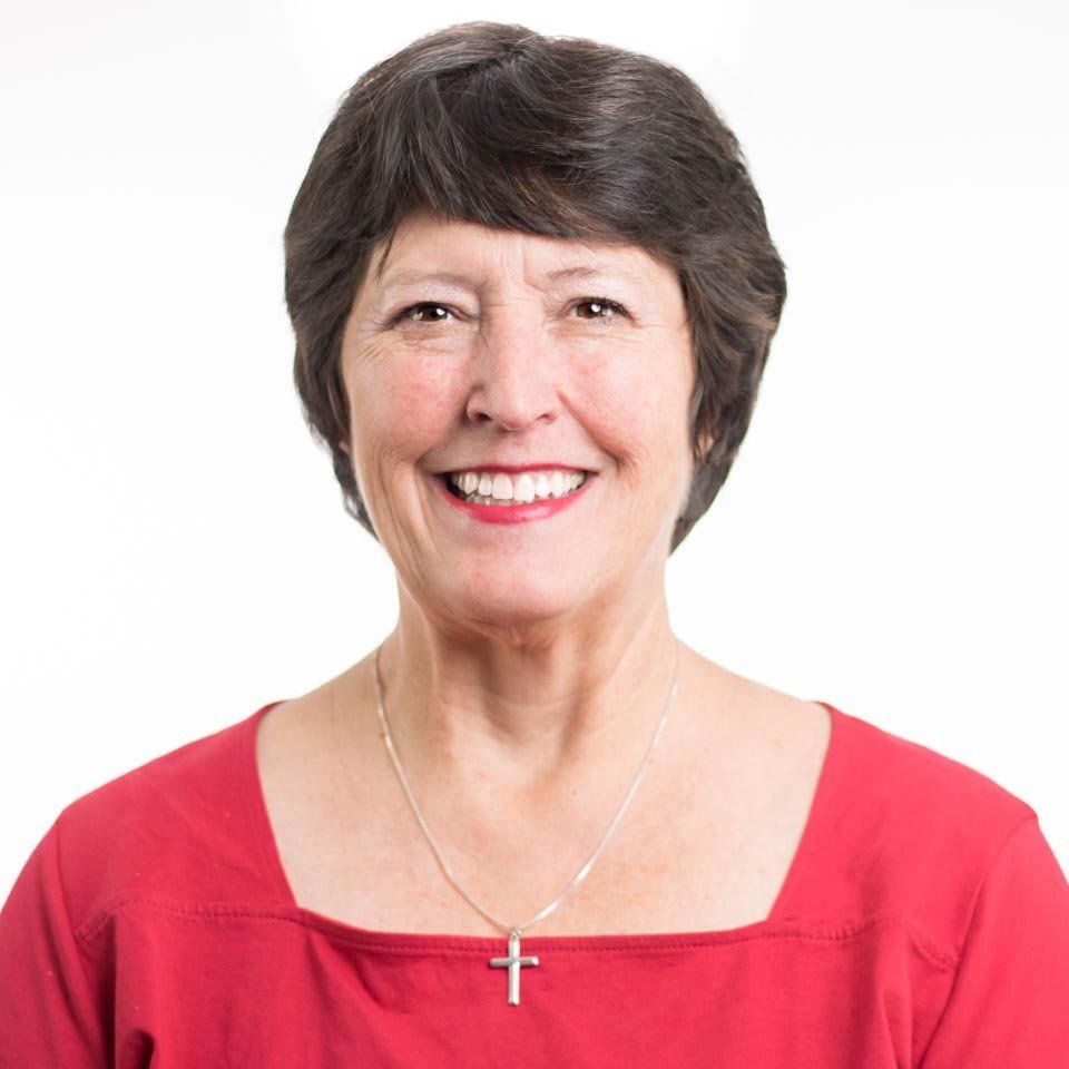Smiling woman in a red top and cross necklace against a white background