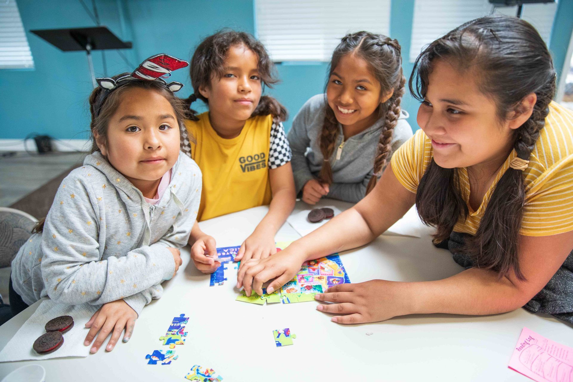 Four children lean over a table, arranging colorful pieces on a white surface in a classroom.