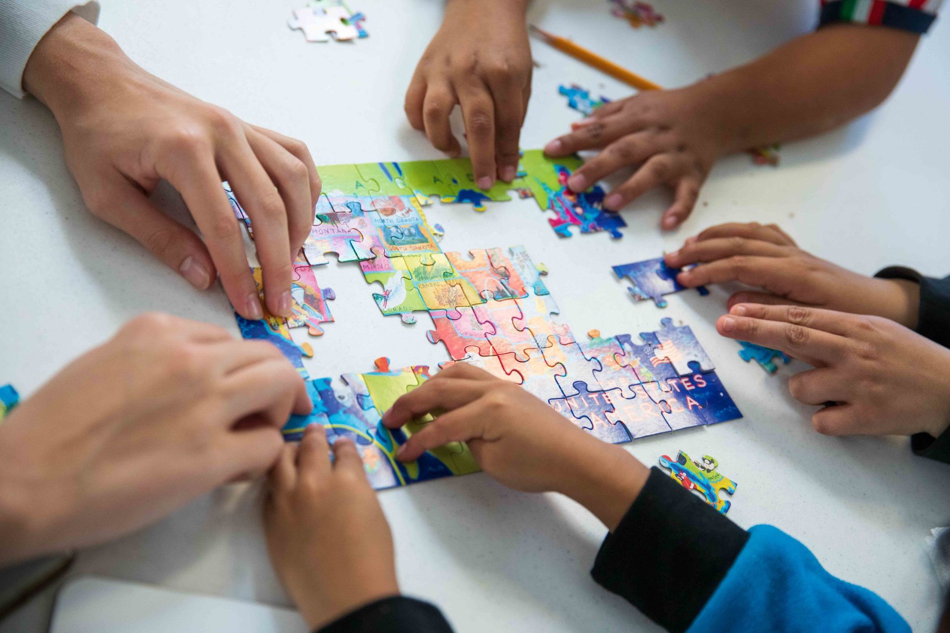 Hands assembling a colorful jigsaw puzzle together on a white table