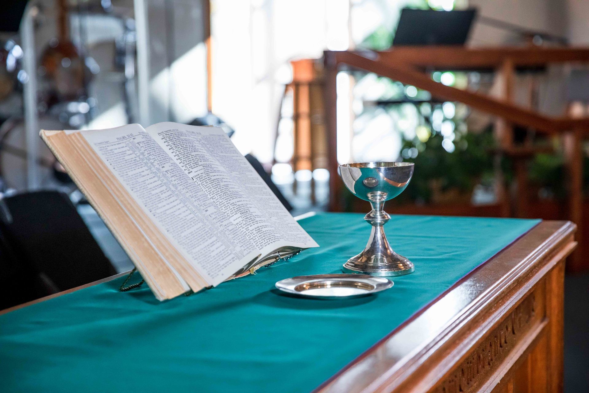 Open book on a teal cloth-covered table beside a chalice in a church-like setting