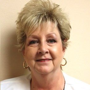 A woman wearing earrings and a white jacket smiles for the camera