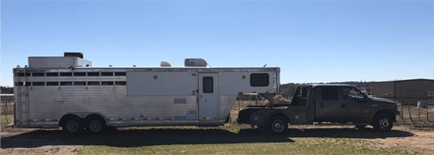 A gray truck towing a silver livestock trailer on a sunny day.
