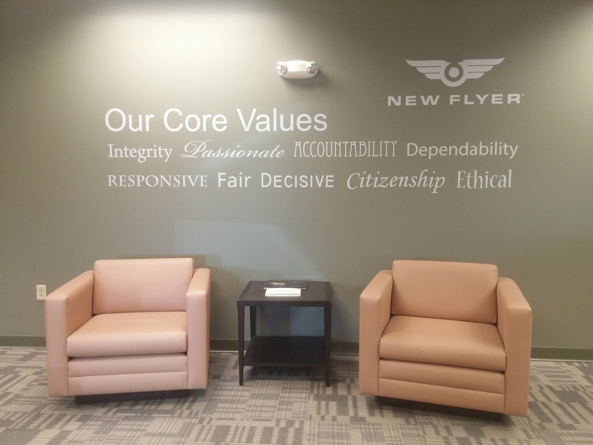 Lobby wall with “Our Core Values” sign, two tan chairs, and a small black table