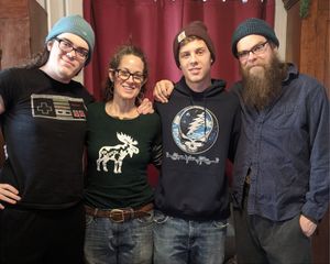 Four people standing together indoors, smiling in front of red curtains.