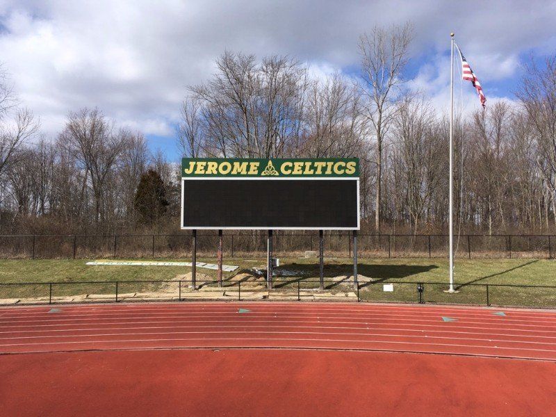 Jerome A. Celtics scoreboard beside a red track with an American flag and leafless trees