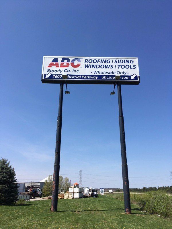 Billboard for ABC Roofing and Siding over a grassy roadside field under a clear blue sky