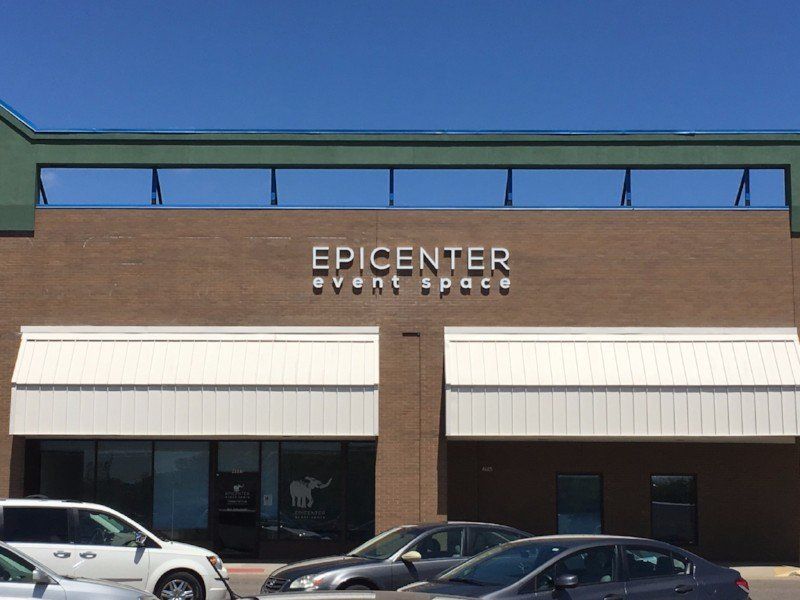Storefront sign reading “EPICENTER event space” on a tan building with parked cars outside.