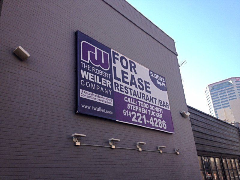 Purple leasing sign on gray building wall for a restaurant/bar, with phone number and website.