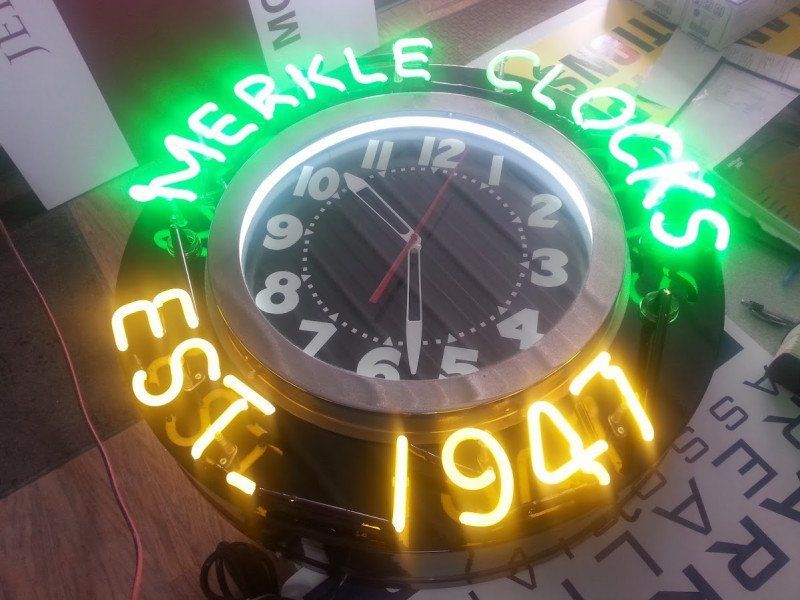 Neon clock sign reading “Merrke Cocks Est 1941” above a round wall clock