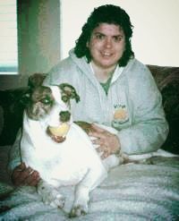 Woman seated on a couch petting a brown and white dog with a tennis ball in its mouth.