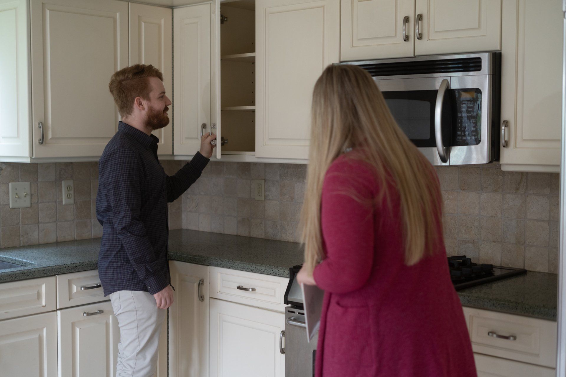 A man and a woman are standing in a kitchen looking at cabinets.