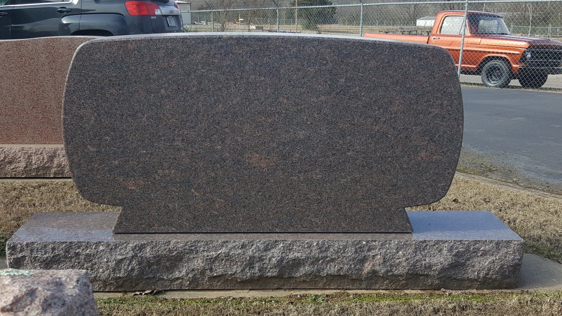 A gravestone in a cemetery with a truck in the background.