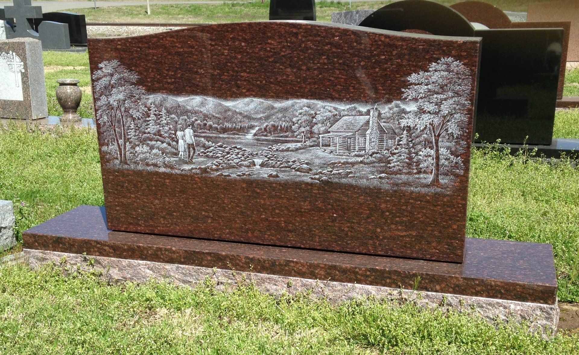 A gravestone in a cemetery with a landscape on it
